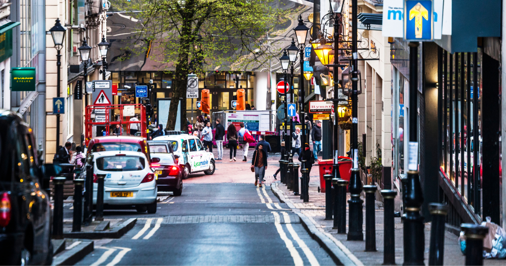UK high street with cars and people walking.