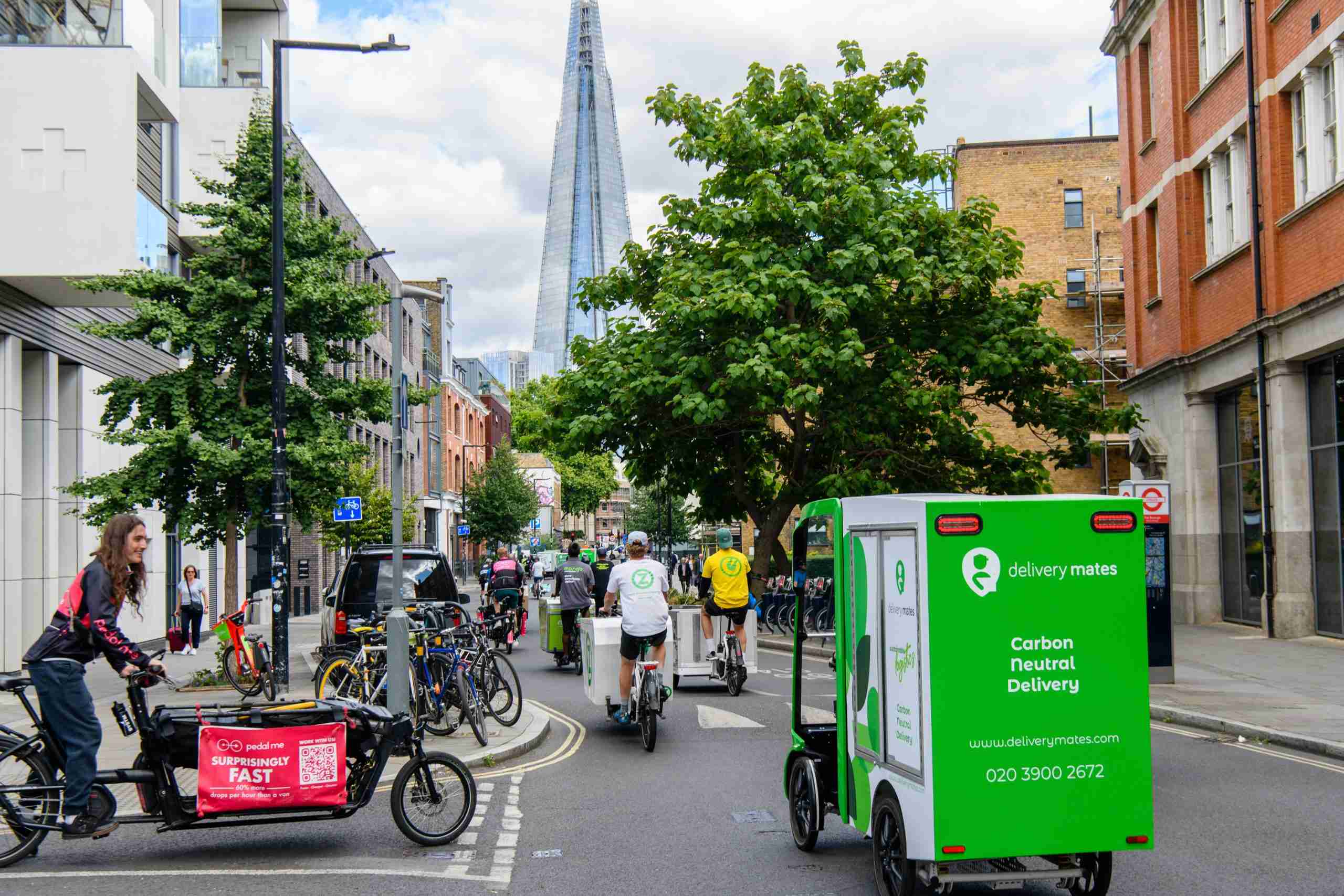 Cargo bike convoy heading down a tree lined London street towards The Shard which is visible in the distance