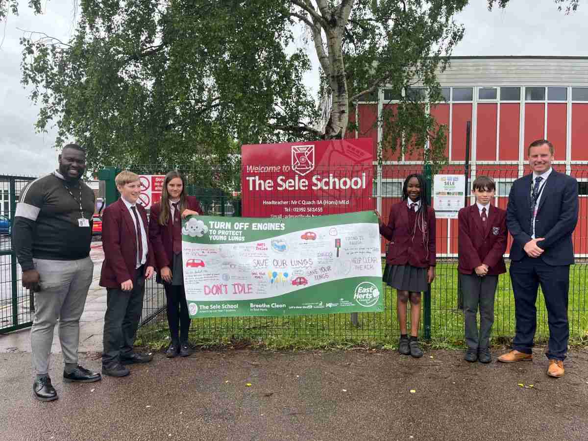 Four pupils standing with two teachers next to a banner which they have hung on their school railings to alert people to the dangers of air pollution.