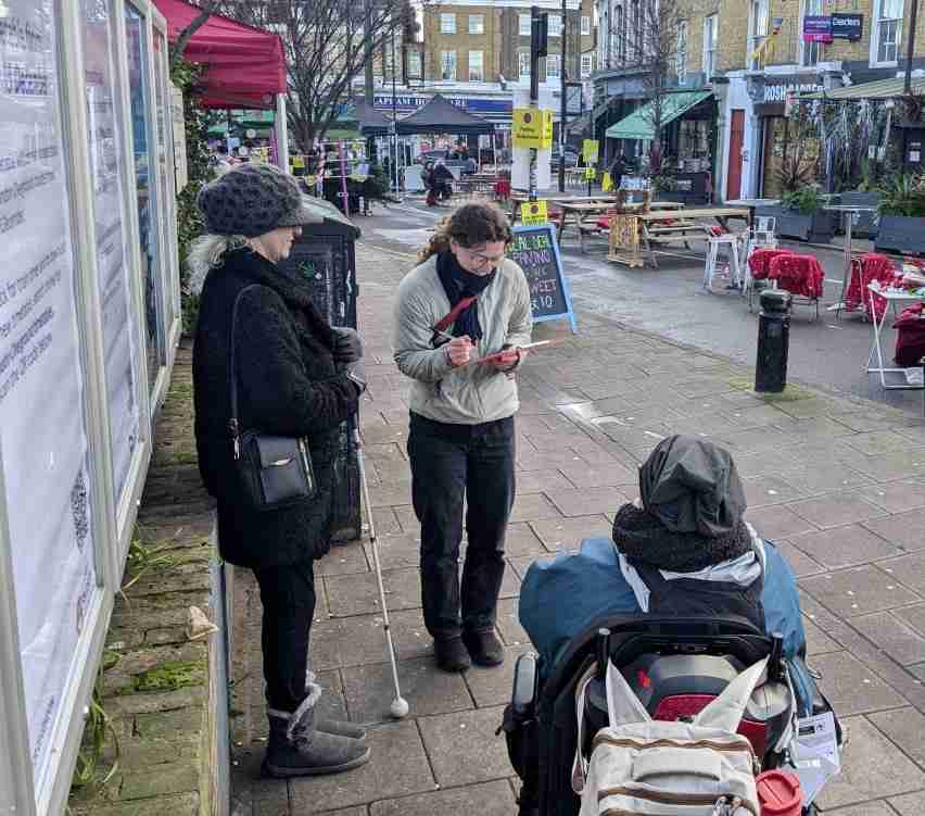 Three people on the street. One woman has a clipboard taking feedback notes. The other two people are members of the Accessibility Working Group.