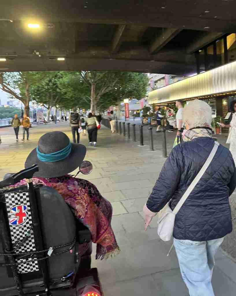 Two women walking away from the camera. They are walking along the South Bank under a bridge.