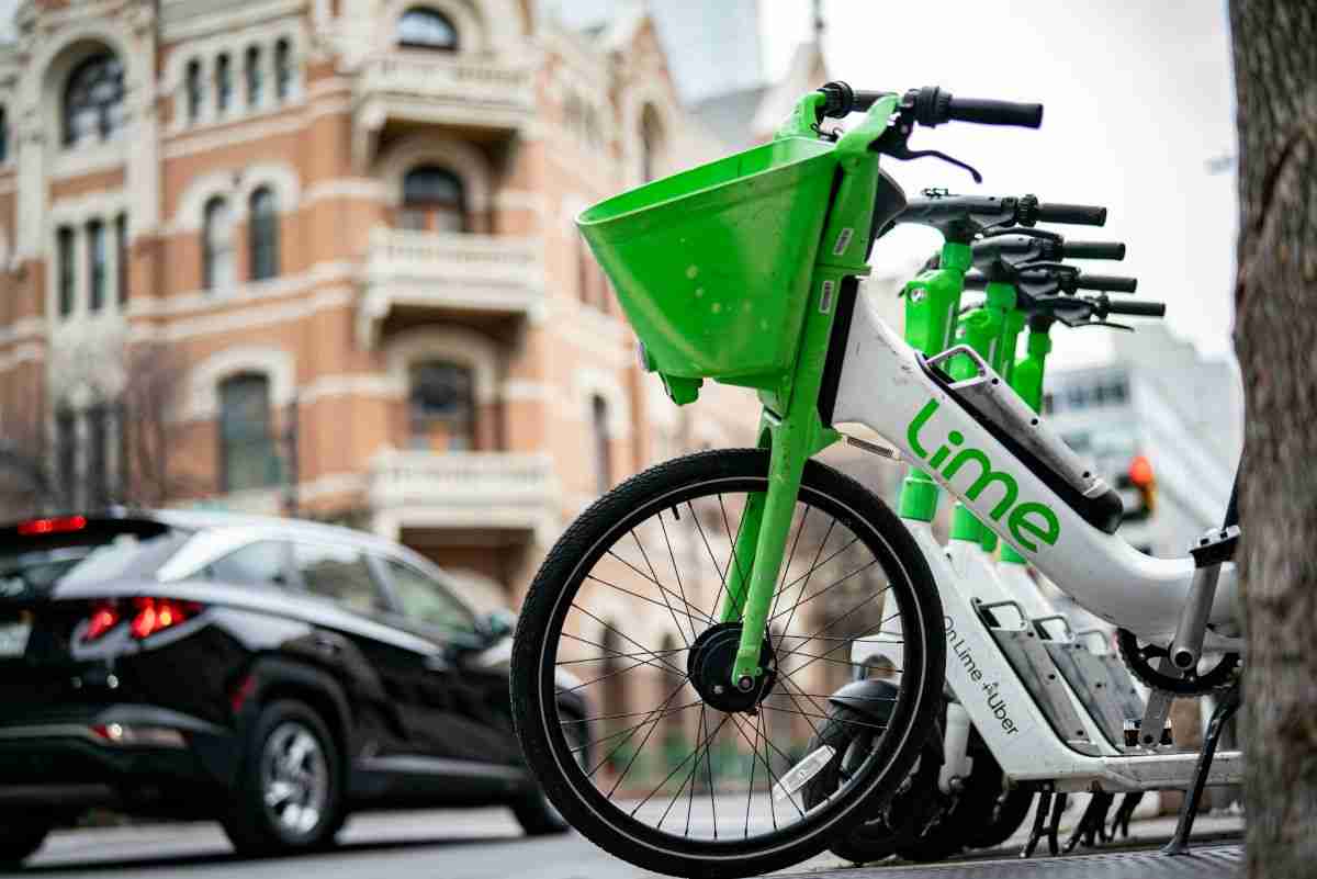 Close up of Lime Bikes parked in a London street. In teh background there is a red brick, Victorian mansion block an din the middle distance a black car is passing by.