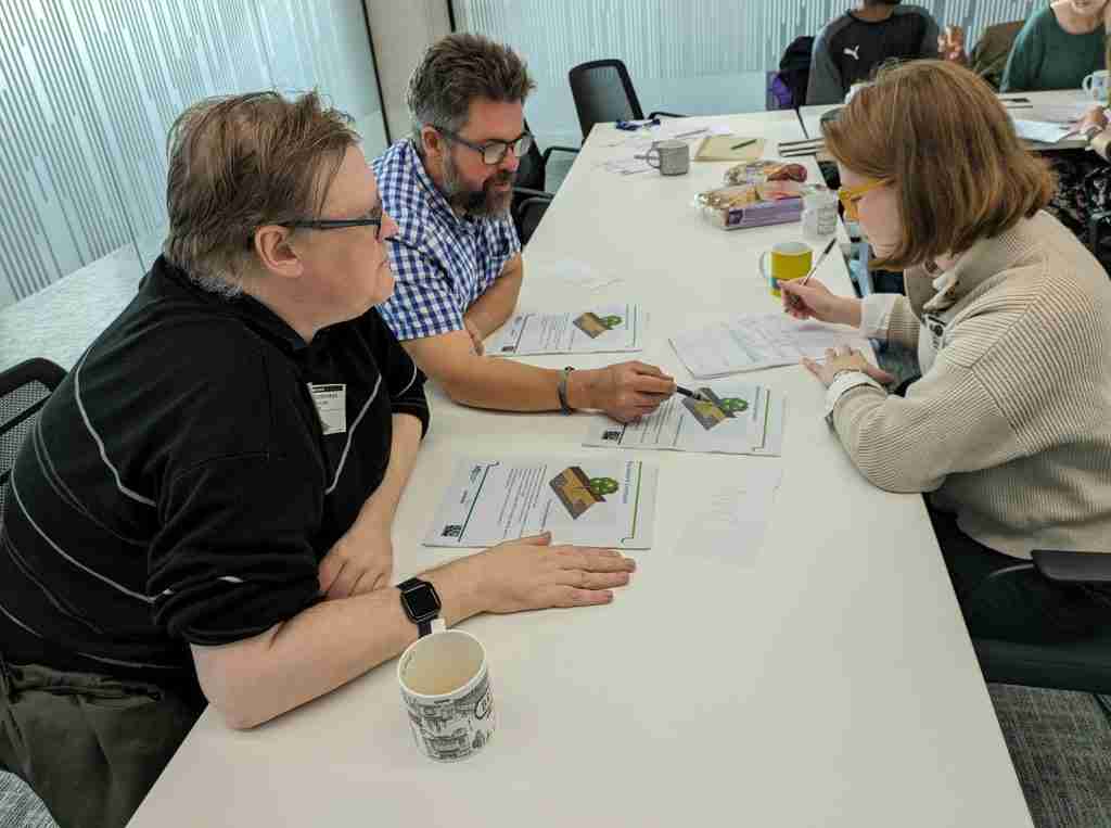 The photo shows an MP Smarter Travel consultant working with two members of the Accessibility Working Group in an office setting. They are looking at and discussing plans about landscaping a street in the London Borough of Lambeth.