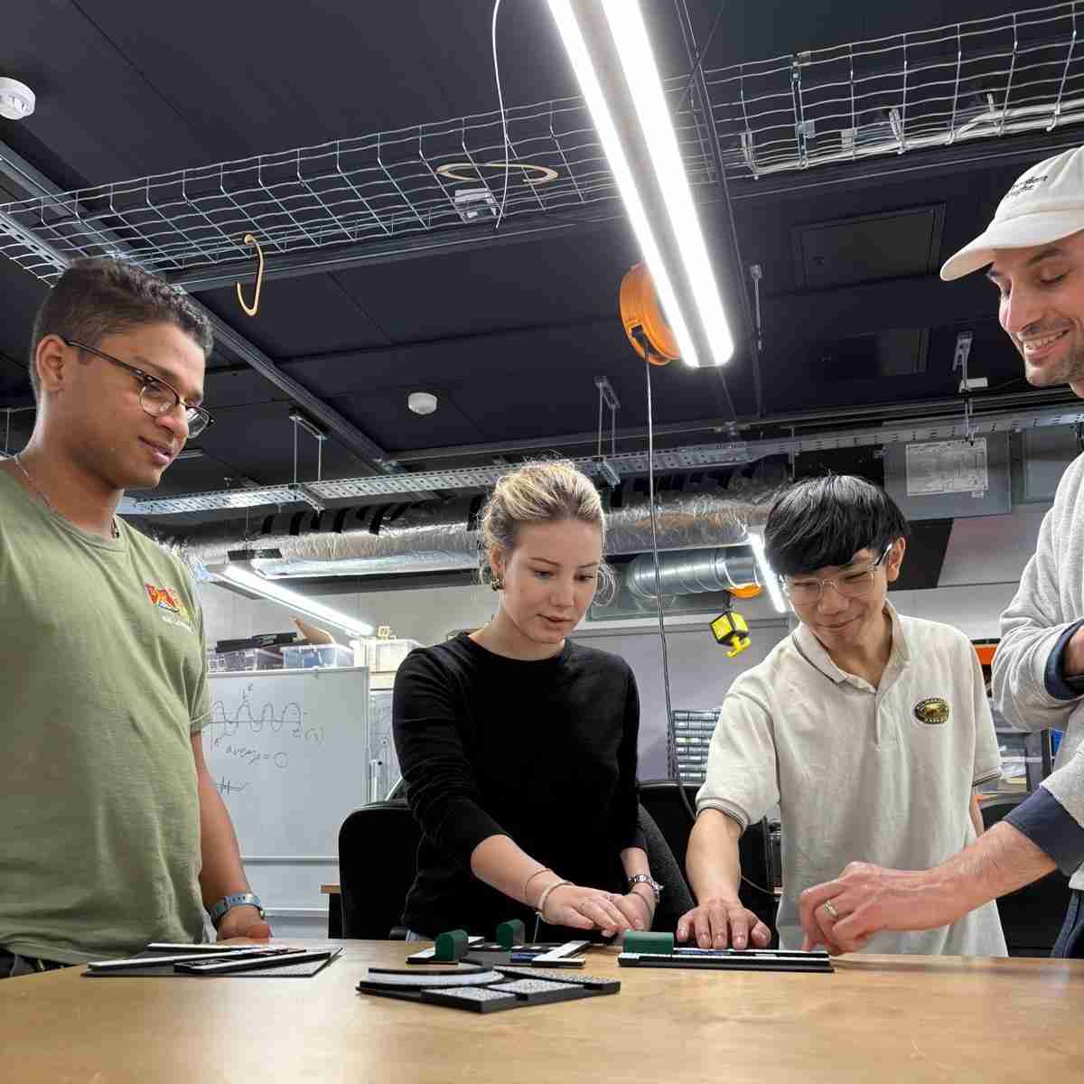 Four researchers in a lab at The Engineering Design Institute, London (TEDI) reviewing models of street infrastructure which have been made to help disabled people, particularly people with vision impairments, take part in meaningful local government engagement exercises about street design.