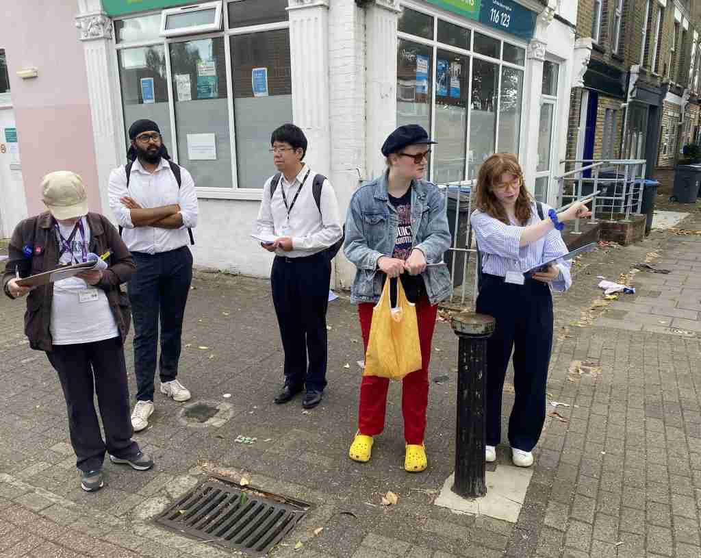 Photo shows a group of five people out on the street commenting on street layout and the improvements that could be made. Two of the people have clipboards and the taking down the comments. 